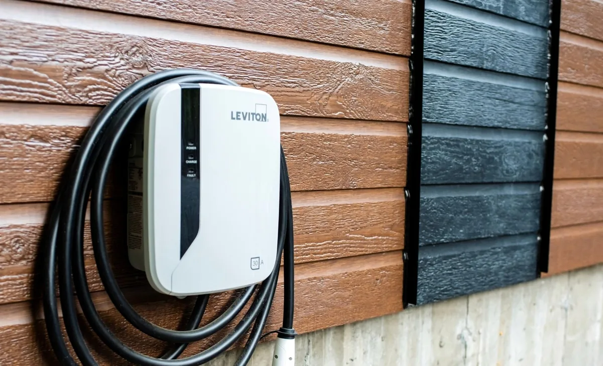 Leviton EV charger mounted on brown wood siding, with the charging cable coiled on the unit